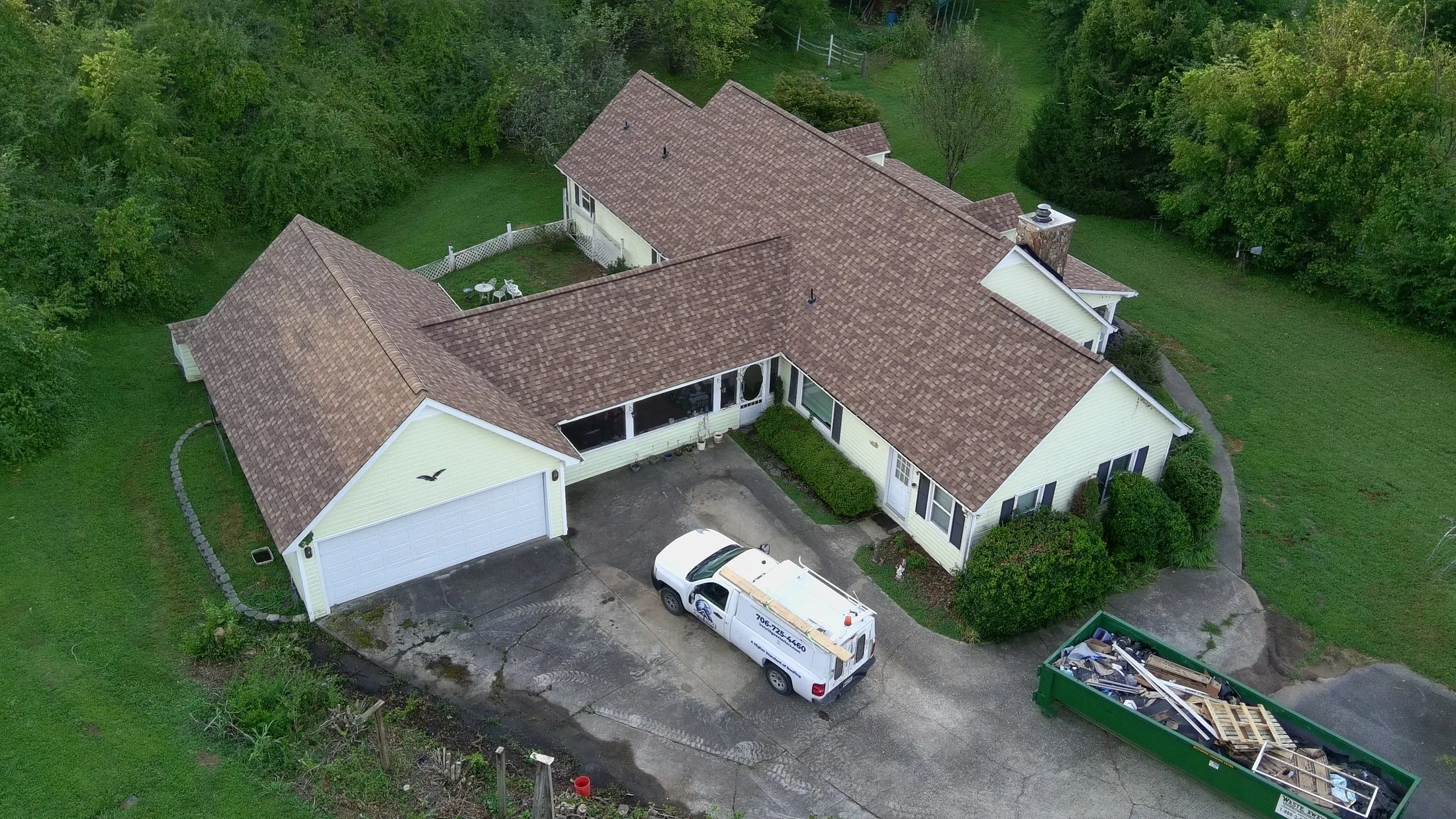 Aerial view of a newly installed brown shingle roof, with the Iron Ridge truck and roll-off dumpster on site